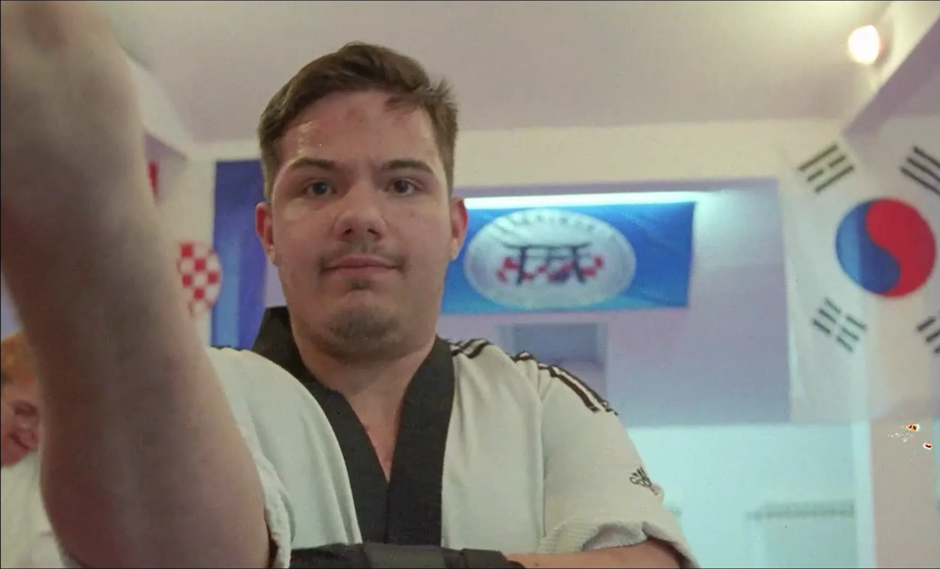 Blackbelts — a Para Taekwondo athlete facing the camera in the dojang, club banner behind.