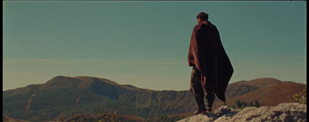 With Blessings On Your Way — a cloaked figure on a rocky ridge above a mountain range.