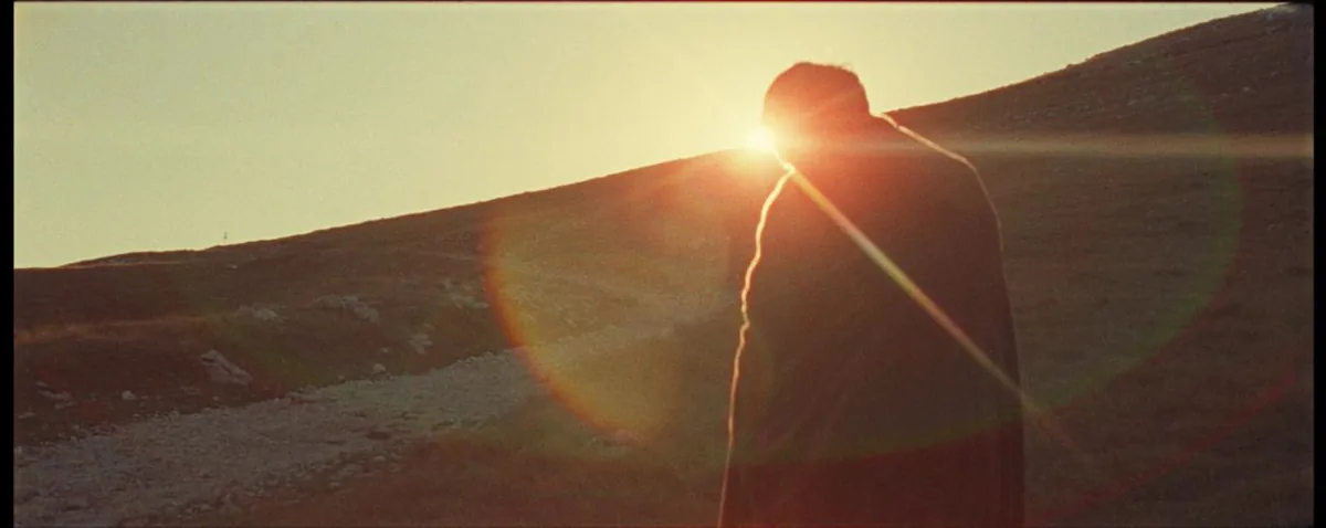 With Blessings On Your Way — the cloaked figure silhouetted against a low sun cresting a ridge.